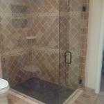 RECESSED SHOWER WITH TRAVERTINE TILE SET AT DIAGONAL AND FRAMLESS GLASS ENCLOSURE VENETIAN BRONZE HARDWARE AND TRIM